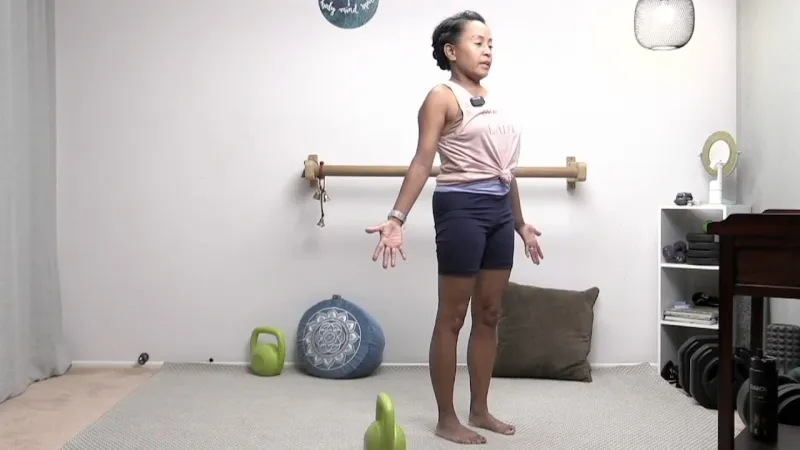 Instructor leading a virtual workout from a home studio with kettlebells and a barre
