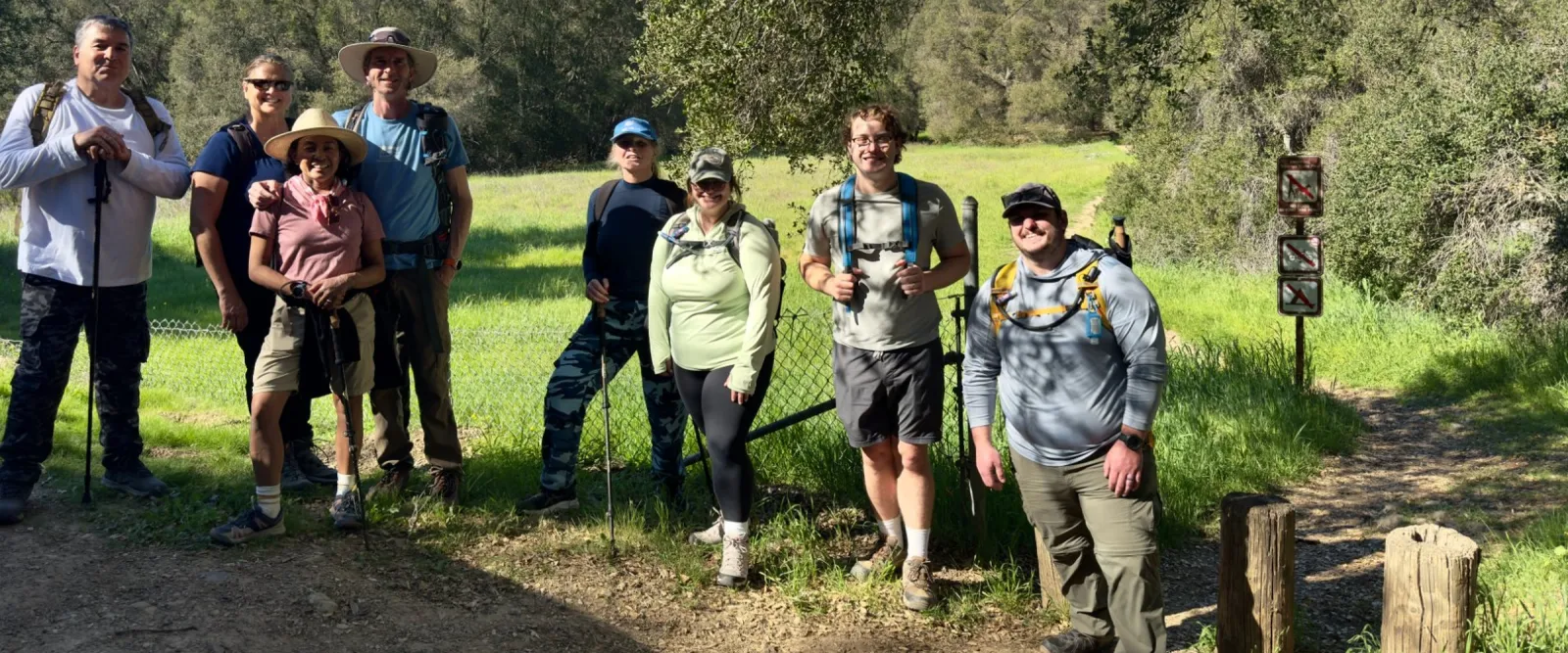 Group of nine hikers with trekking poles smiling together on a trail